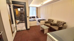 Une chambre d’hôtel comprenant un lit, deux fauteuils, une table basse, une table avec un plateau en verre, et une salle de bain avec douche et toilettes.