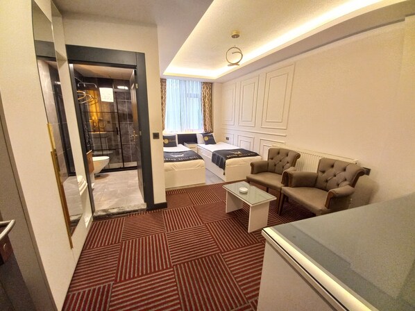 A hotel room with a bed, two armchairs, a coffee table, a glass-top table, and a bathroom with a shower and toilet.