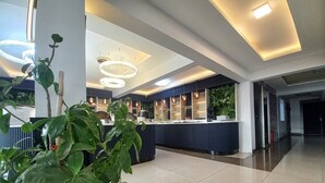 Un hall d’hôtel moderne avec un comptoir d’accueil, des luminaires suspendus et une grande plante.
