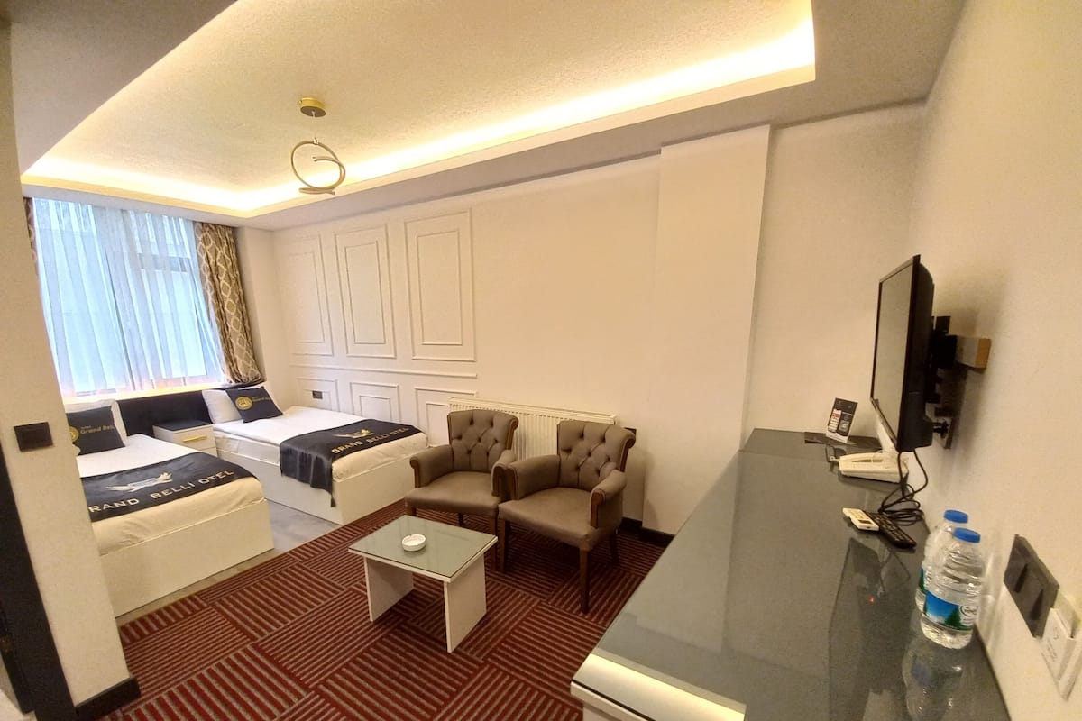 A hotel room with a bed, two armchairs, a small coffee table, a TV, and a desk with a computer and phone.