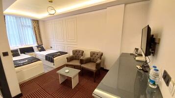 Une chambre d’hôtel comprenant un lit, deux fauteuils, une petite table basse, un téléviseur et un bureau avec un ordinateur et un téléphone.