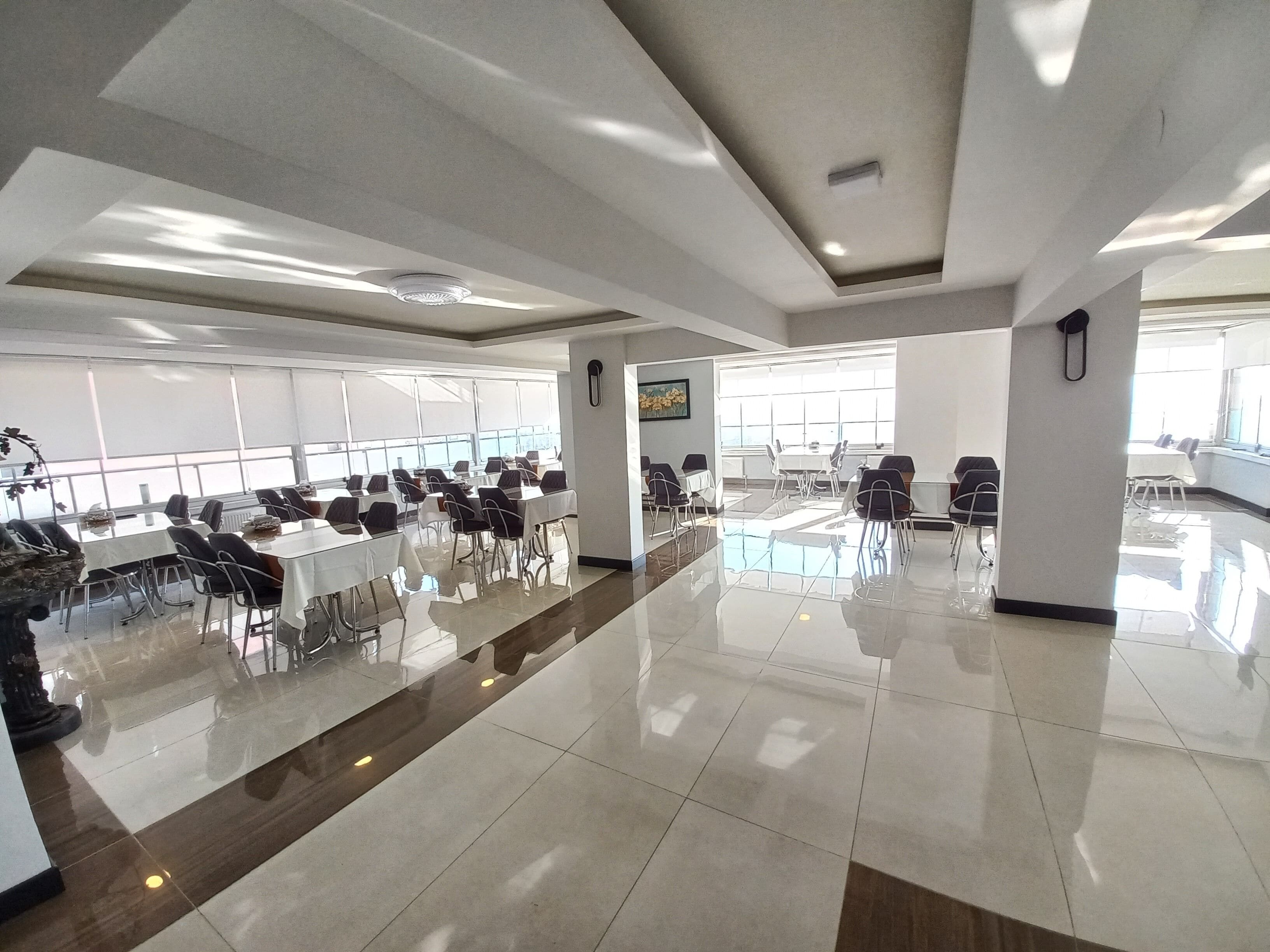 A spacious conference room with multiple tables and chairs, large windows, and a polished floor.