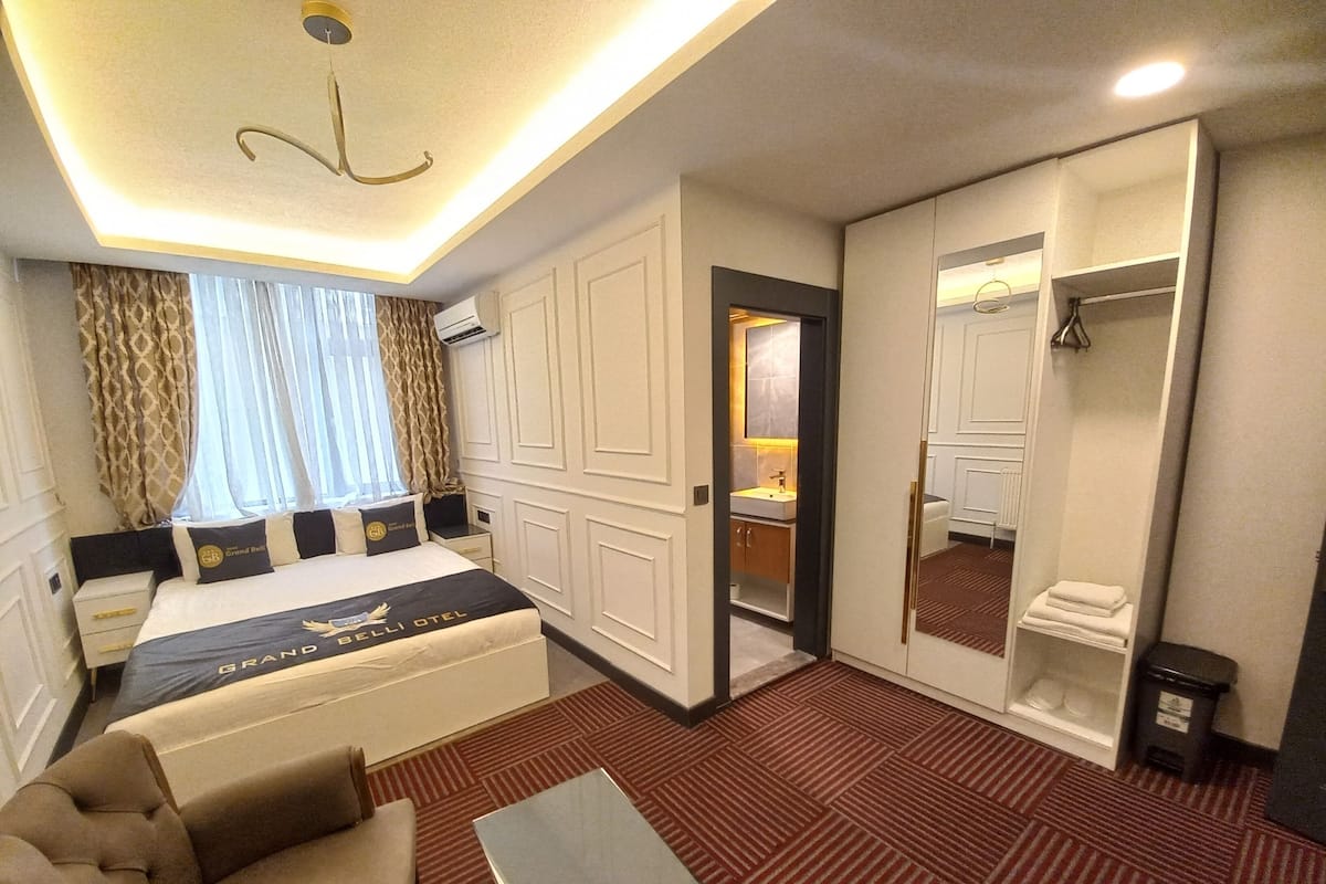 A hotel room with a bed, a sofa, a small table, a walk-in closet, and a bathroom.