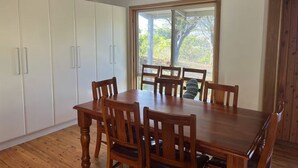 A dining area with a wooden table and chairs, white cabinets, and a large window with a view of trees. - 15% Off Weekly | Coastal-View Cypress Beach House (Island Beach)