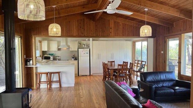 A spacious living area with a black leather sofa, wooden flooring, and a kitchen in the background. - 15% Off Weekly | Coastal-View Cypress Beach House (Island Beach)