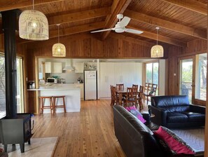 A spacious living area with a black leather sofa, wooden flooring, and a kitchen in the background.