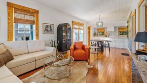 A spacious living area with a sofa, armchair, and coffee table, wooden flooring, and a kitchen in the background. - Welcome to The Schoolhouse – A charming cottage in historic Monticello, Florida. (Monticello)