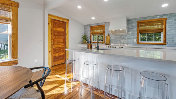 A modern kitchen with a white island, wooden bar stools, and a large window with blinds. - Welcome to The Schoolhouse – A charming cottage in historic Monticello, Florida. (Monticello)
