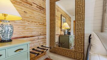 A room with a wooden wall, a large mirror with a geometric frame, a bedside table with a lamp, and a bed with a blanket.