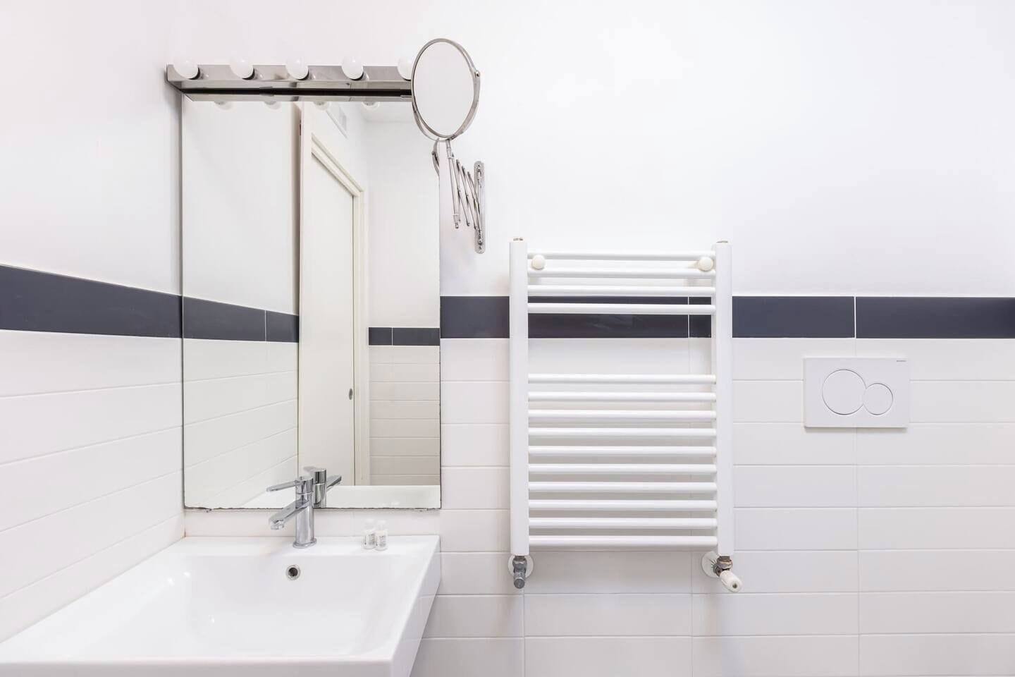 Ein Badezimmer mit Waschbecken, Spiegel, Handtuchhalter und Wandheizung.
