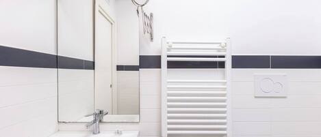 A bathroom with a sink, mirror, towel rack, and a wall-mounted heater.