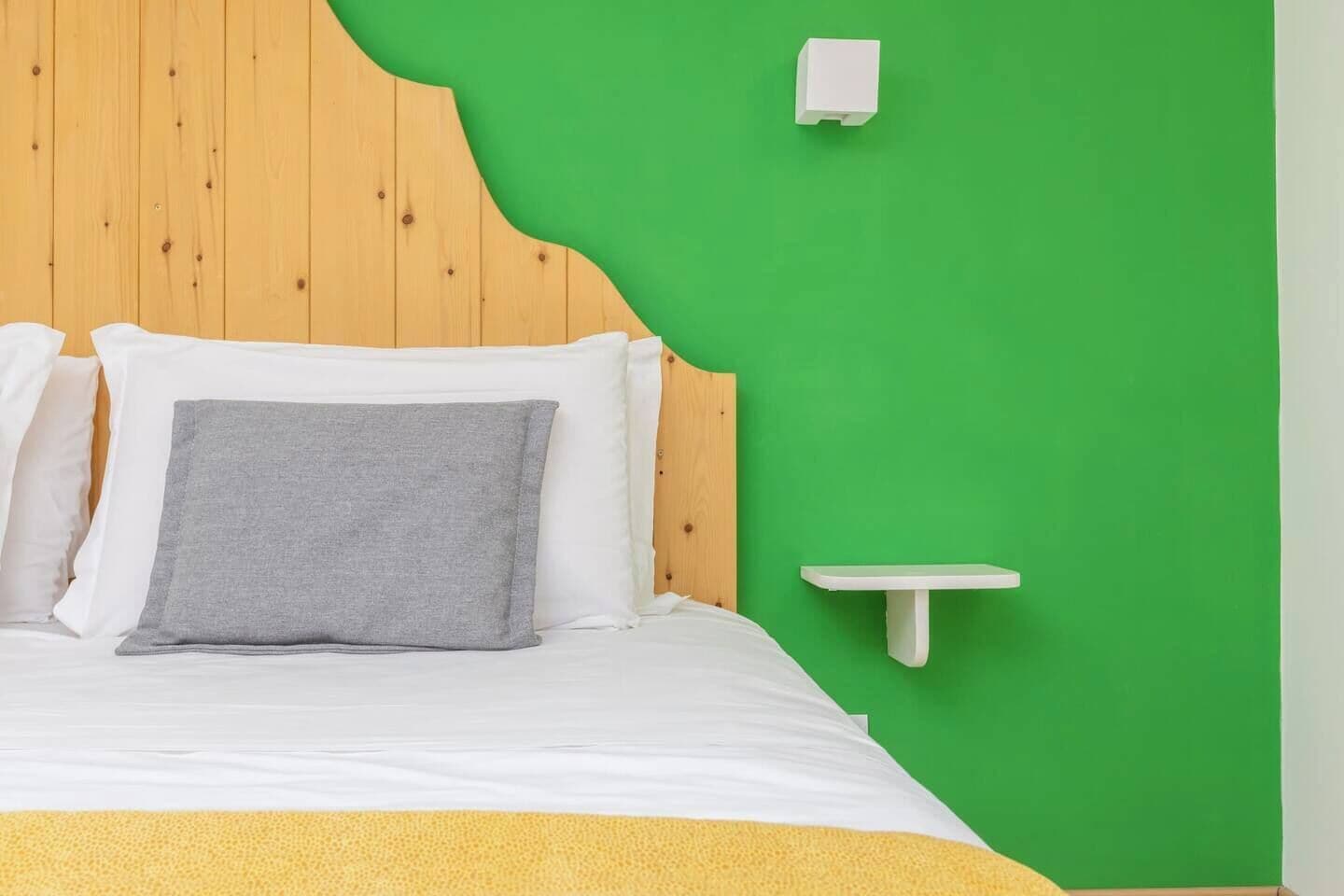 Una cama con almohadas blancas y grises, un cabecero de madera y una pared verde.