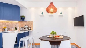 A modern kitchen with blue cabinets, a white island, and a dining area with a round table and white chairs. - Stylish & Elegant Flat With Terrace (Sorrento)