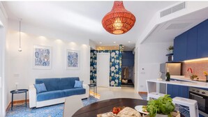 A modern living room with a blue sofa, a dining table with food, a kitchen area, and a red hanging light fixture. - Stylish & Elegant Flat With Terrace (Sorrento)
