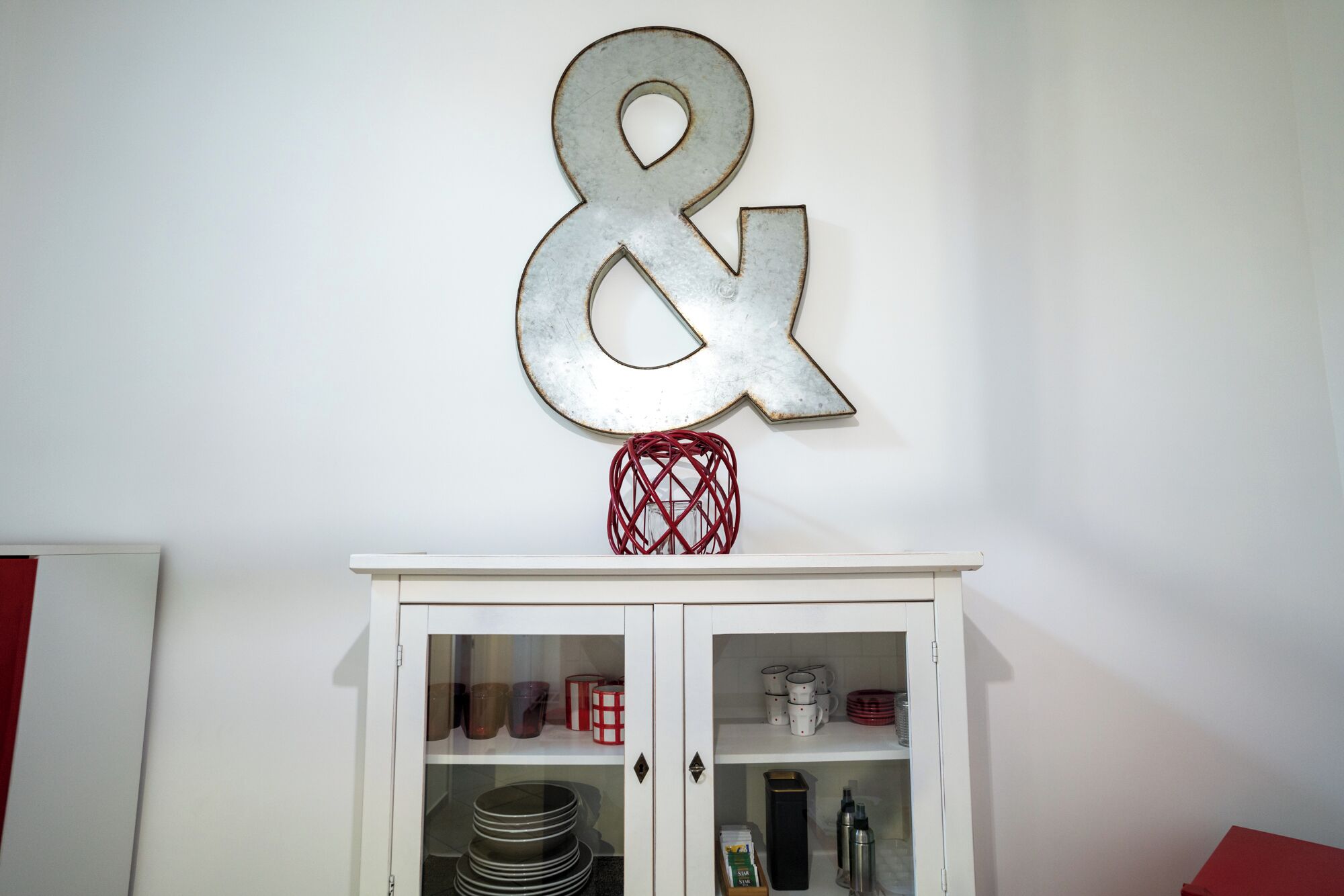 Un meuble blanc avec des portes en verre, contenant des ustensiles de cuisine, et une enseigne décorative en métal au-dessus.