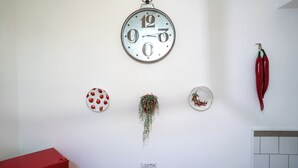 Una pared con un reloj, una caja roja, un enchufe y elementos decorativos como chiles y una planta.
