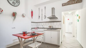 Una cocina moderna con armarios blancos, una mesa roja y una estufa. Hay decoraciones en la pared, incluyendo un reloj y un cartel que dice 