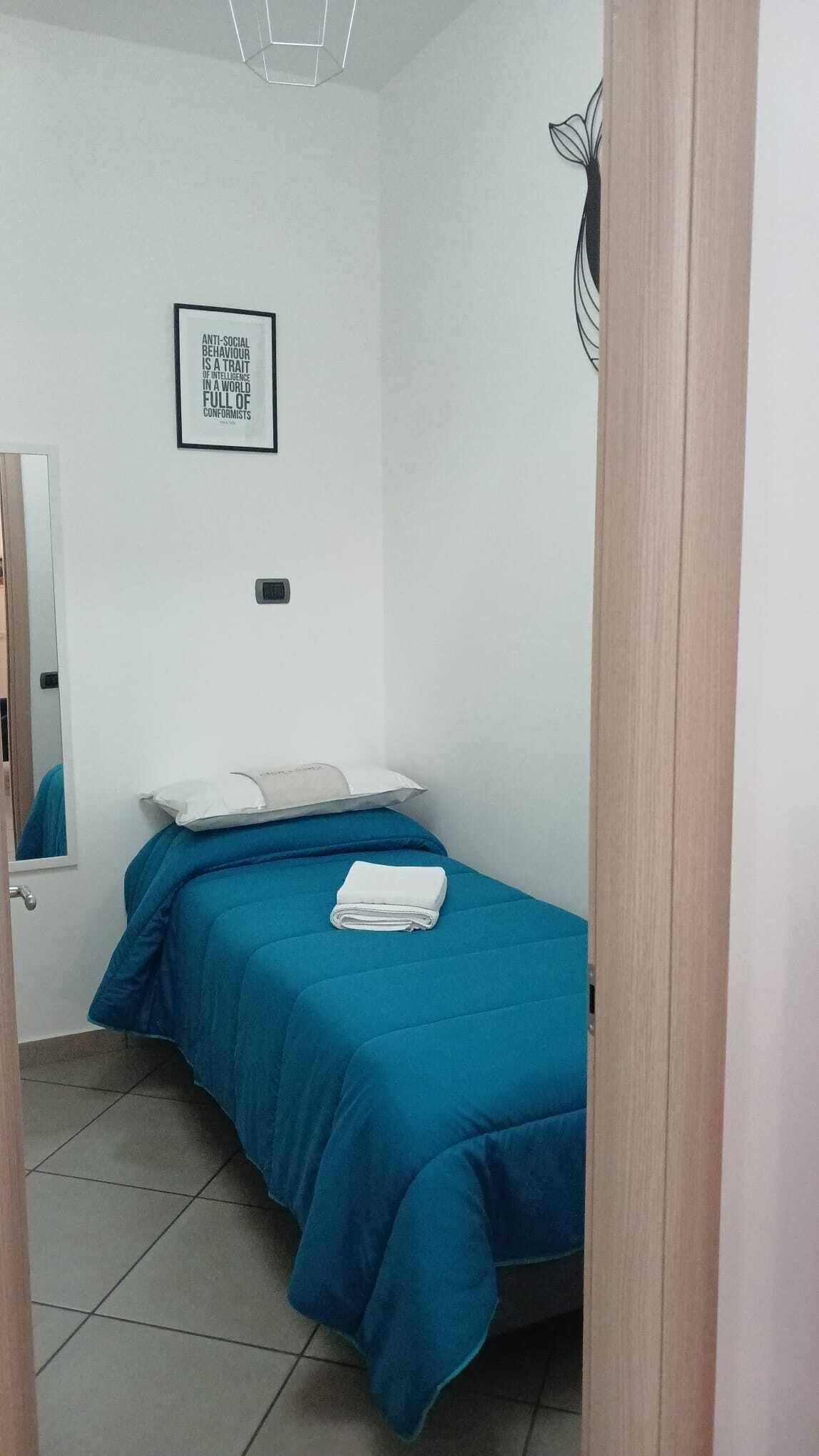 A bedroom with a bed, a mirror, a wall-mounted light, and a framed quote.