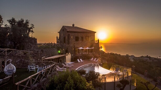 A stone building with a pool and lounge chairs, overlooking a body of water at sunset. - Villa Breathtaking View Near Nerano (Massa Lubrense)