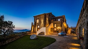 A stone building with a modern design, featuring a car parked in front and a well-lit entrance. - Villa Breathtaking View Near Nerano (Massa Lubrense)