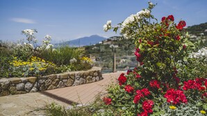 A garden with a stone pathway, red and white flowers, and a mountainous backdrop. - Villa Breathtaking View Near Nerano (Massa Lubrense)