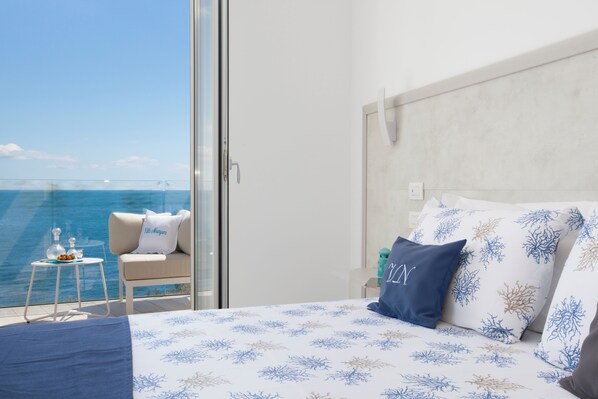 A bedroom with a bed, a chair, and a small table with a view of the sea.