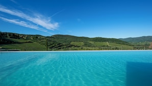 A clear blue pool with a view of rolling hills and a distant village. - Villa Chianti With Infinity Pool And Vineyard View (Greve in Chianti)