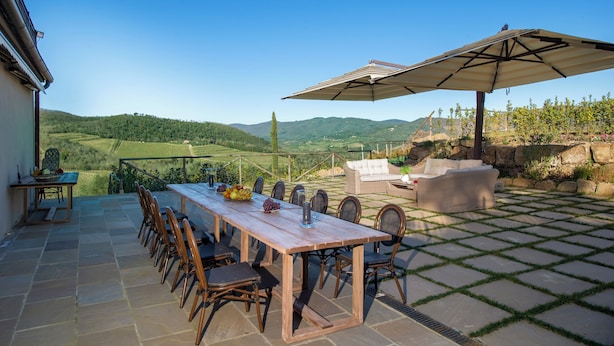 A patio with a wooden table and chairs, an outdoor sofa, and a large umbrella. - Villa Chianti With Infinity Pool And Vineyard View (Greve in Chianti)