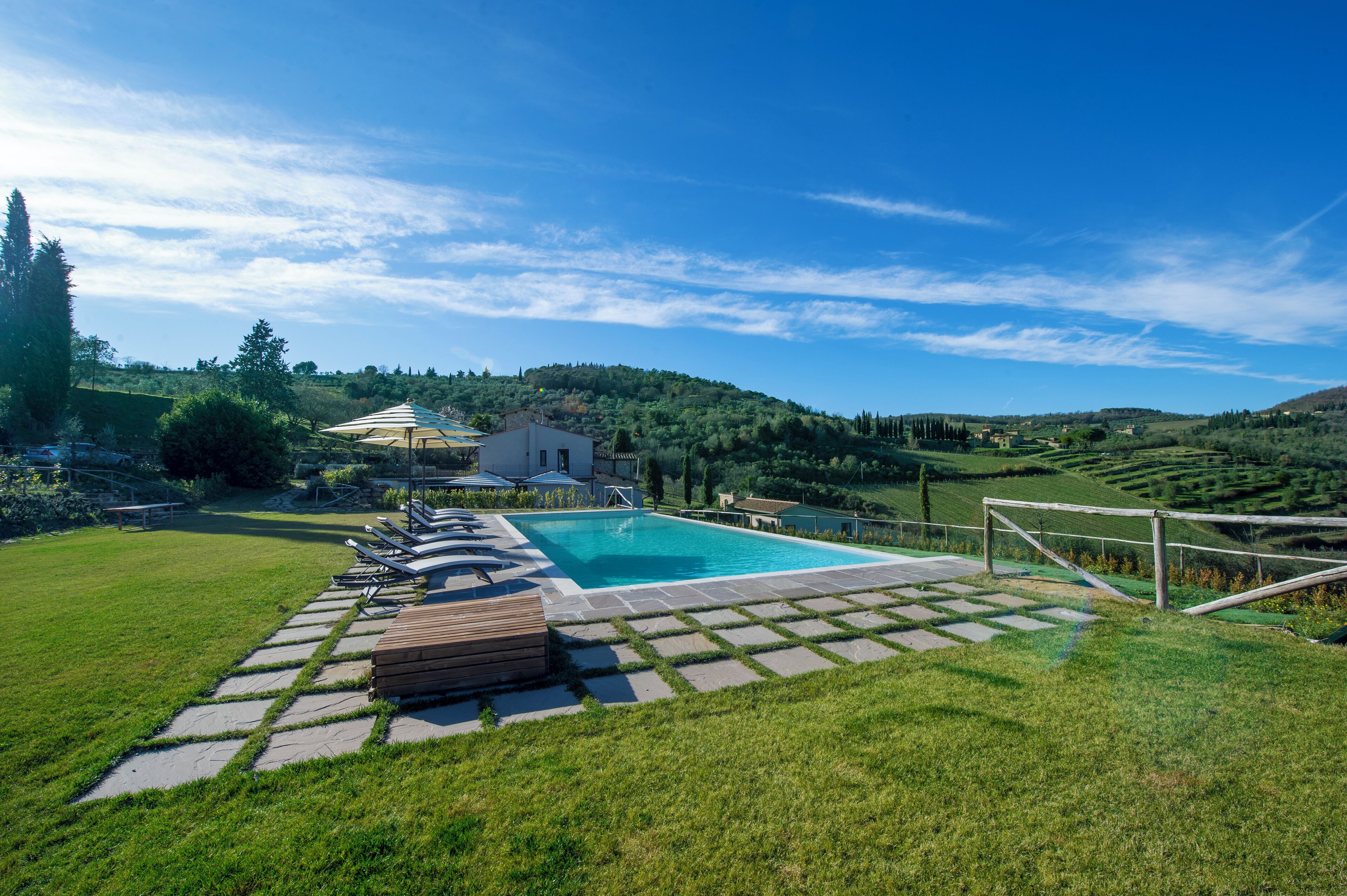 Una piscina con sillones reclinables, una terraza de madera y vistas a colinas ondulantes bajo un cielo despejado.