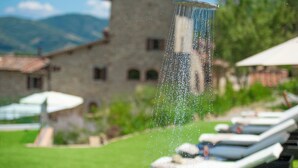Un pommeau de douche laissant jaillir de l’eau, un bâtiment en arrière-plan et un espace piscine avec des chaises longues.