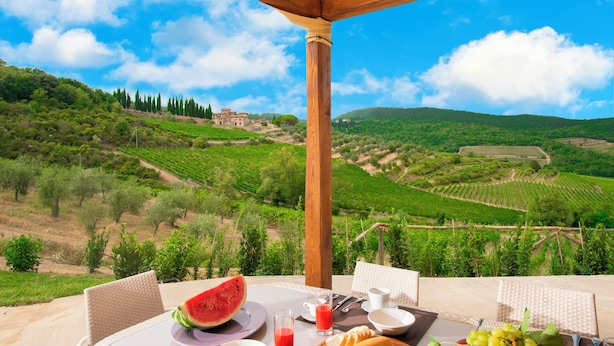 Ein Esstisch, gedeckt für das Frühstück, mit Blick auf Weinberge und ein entferntes Gebäude.