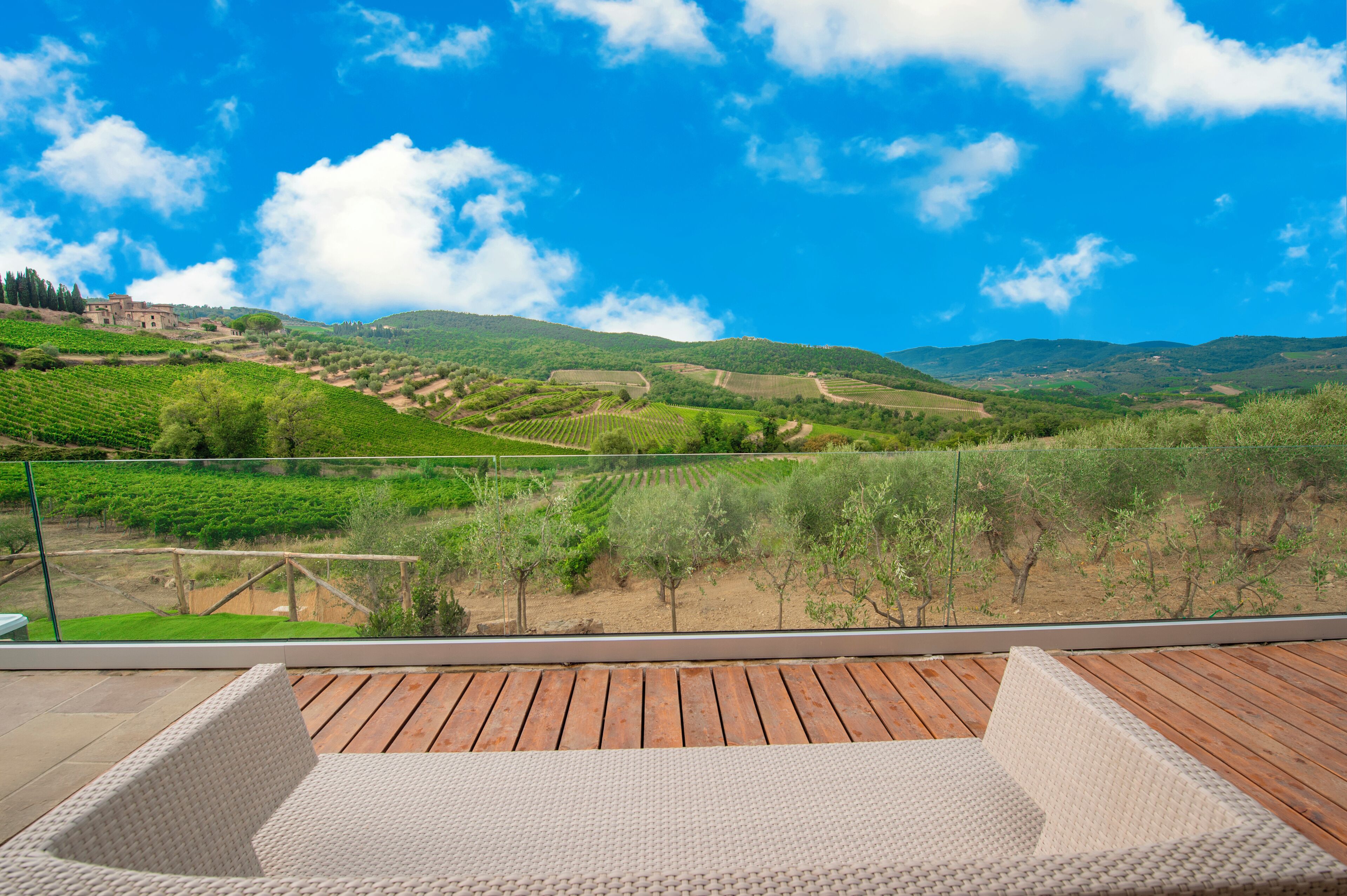 A terrace with wicker furniture overlooking a vineyard and hills.