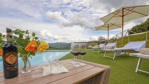 Ein Holztisch mit einer Flasche Comignol, zwei Weingläsern und einer Rosenvase in einer Pool Lounge mit Sonnenschirmen und Liegestühlen.