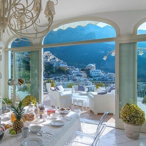 A dining area with a table set for breakfast, overlooking a scenic coastal view with white buildings and mountains. - Villa In Positano With Luxury Spa & Amazing View (Positano)