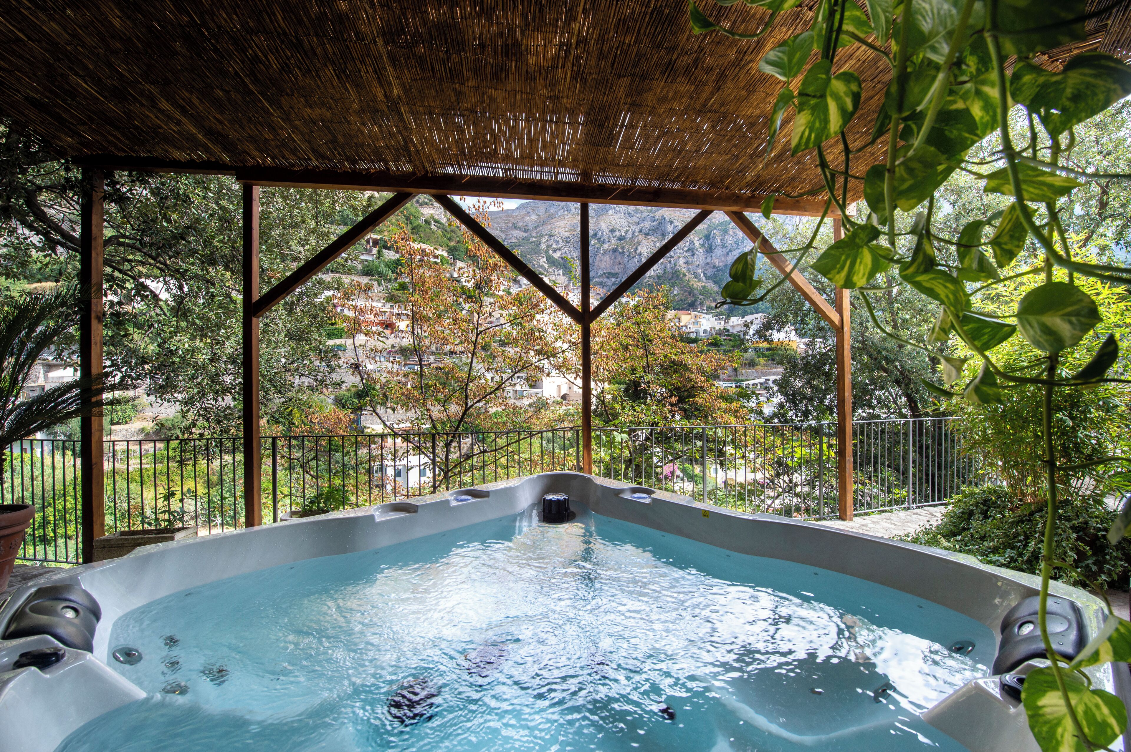A hot tub under a thatched roof with a view of a mountainous landscape.