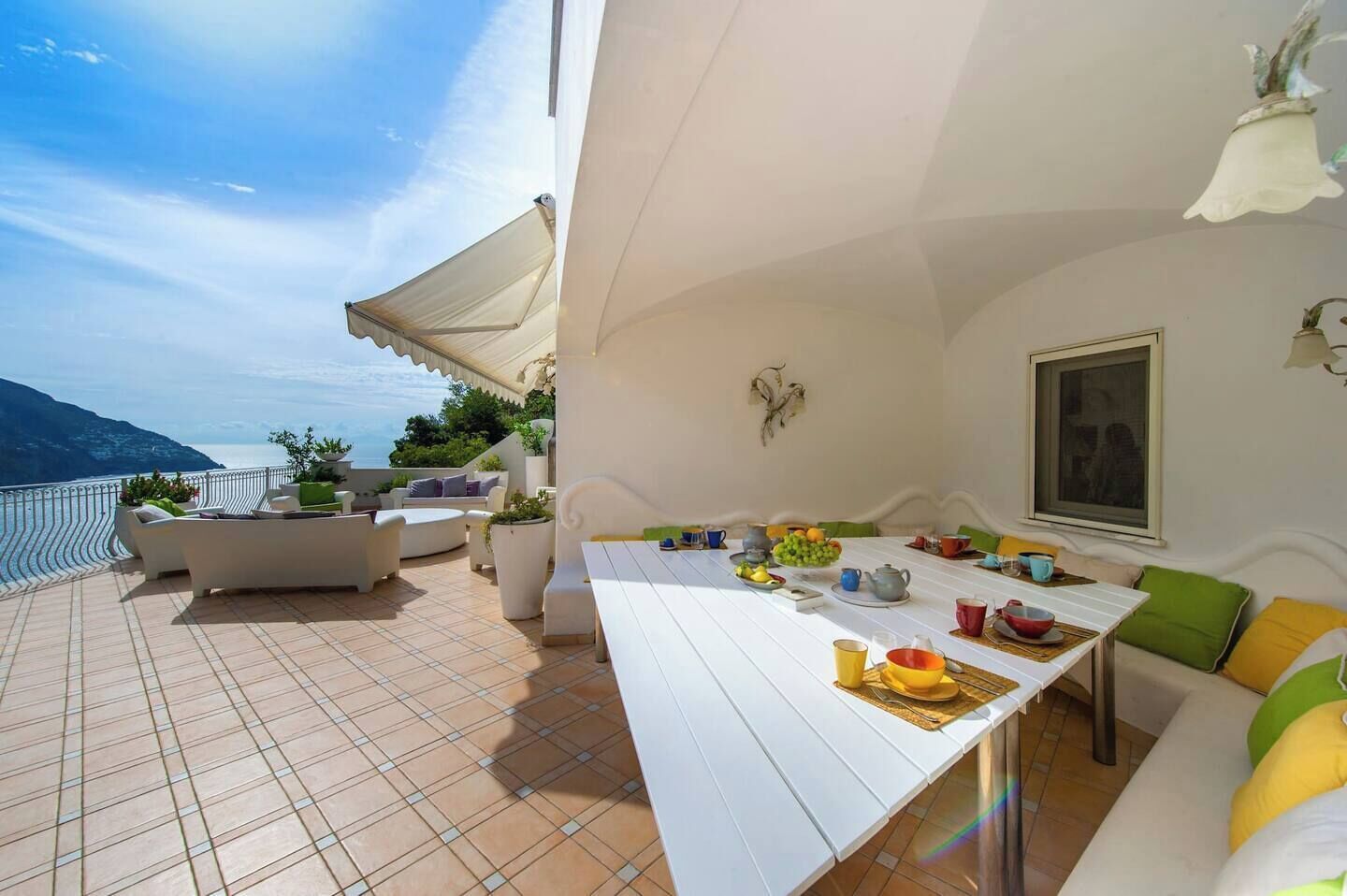 Eine Terrasse mit Esstisch für vier Personen, umgeben von Sofas und Topfpflanzen.