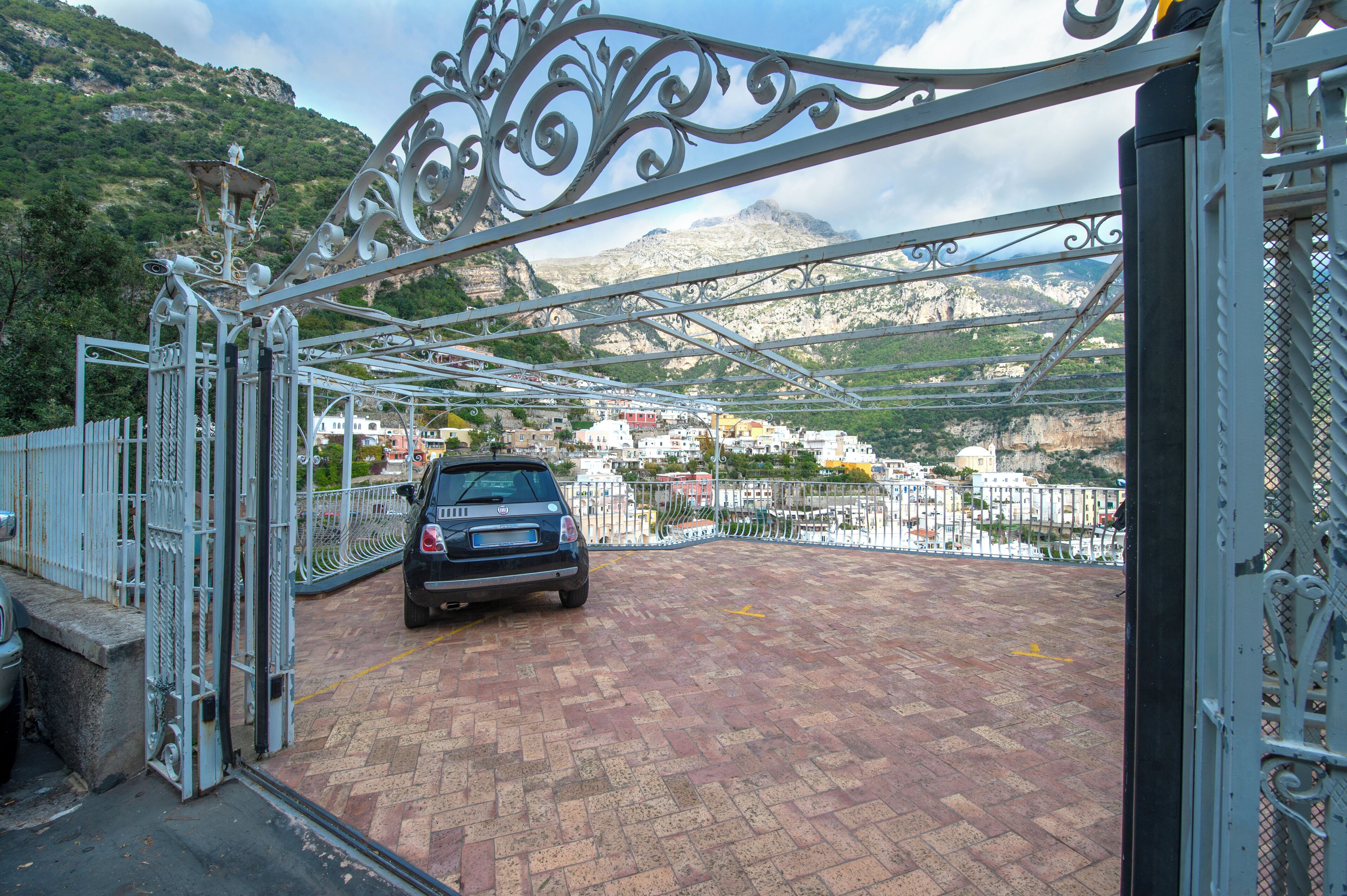 Une voiture est garée dans un parking fermé, offrant une vue sur un paysage montagneux et des bâtiments en arrière-plan.