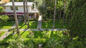 A lush garden with palm trees, a statue, and a building with a balcony.
