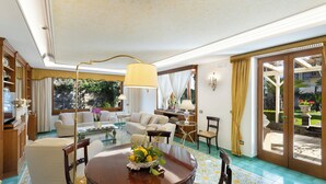 A spacious living room with a round wooden table, comfortable seating, and a large window offering a view of the garden.