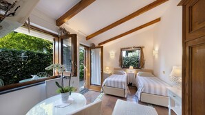 A bedroom with two beds, a balcony with a table and chairs, and a view of greenery outside.