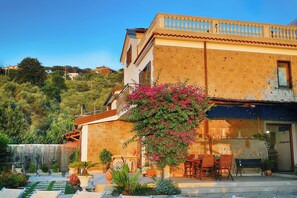 A building with a balcony, a garden with potted plants, and a small outdoor seating area.