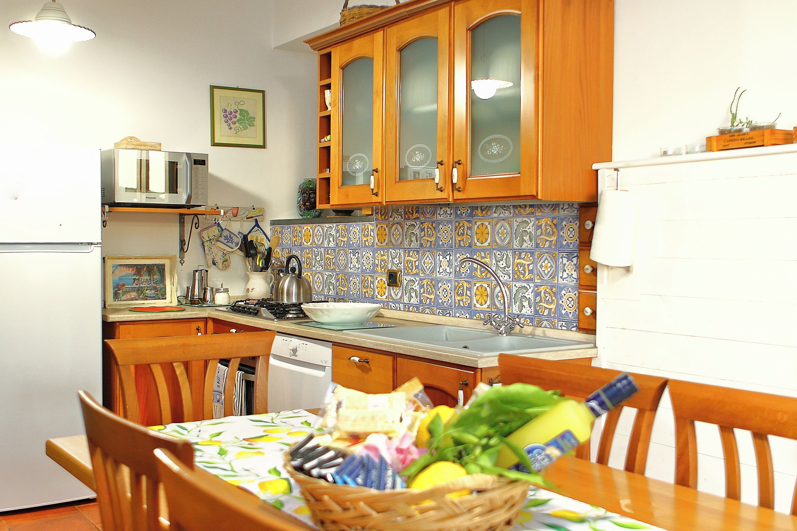 A kitchen with wooden cabinets, a microwave, a sink, and a dining table with a basket of fruit.