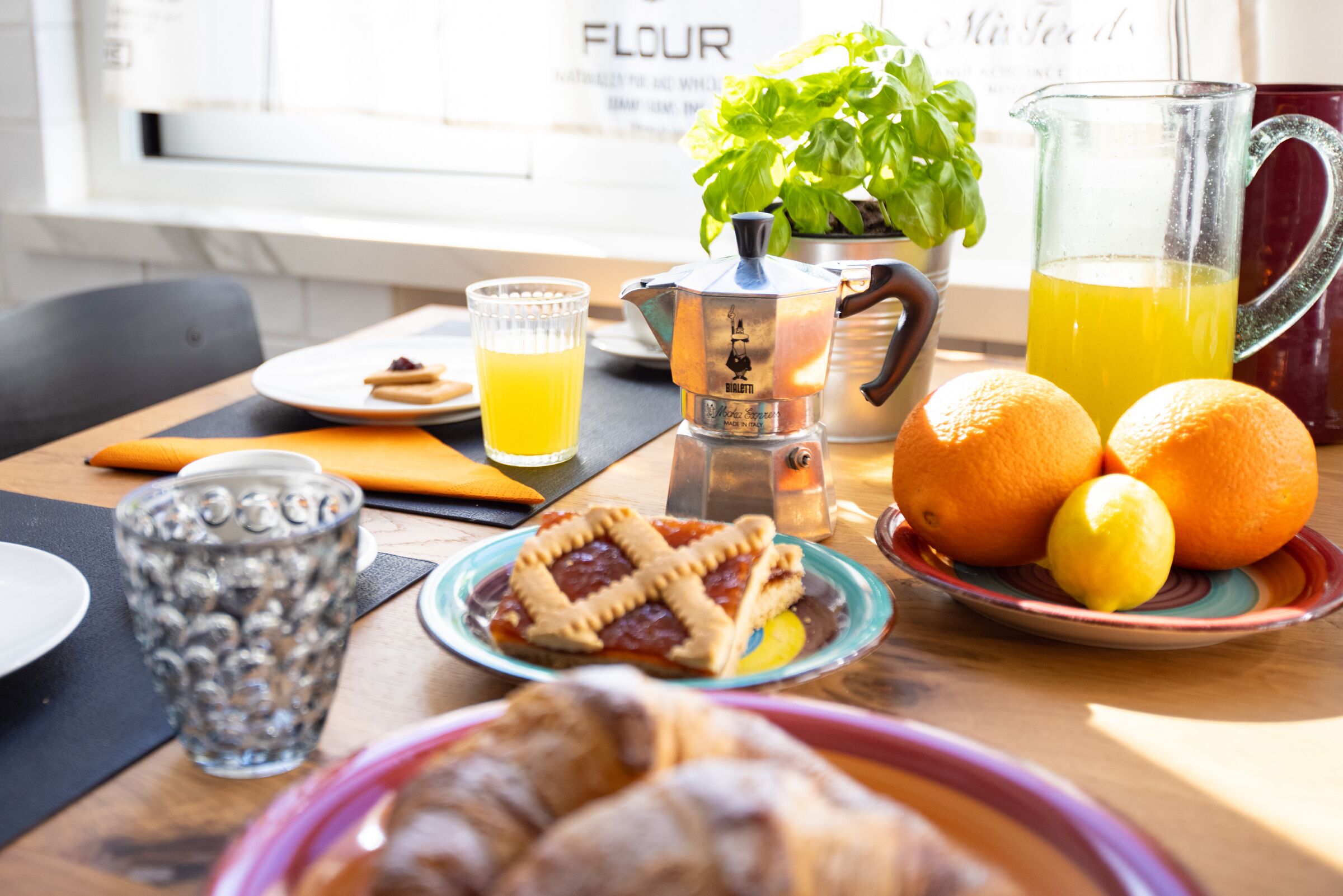 A breakfast table with a pitcher, a glass of orange juice, a plate with a pie, a plate with oranges, and a glass of water.