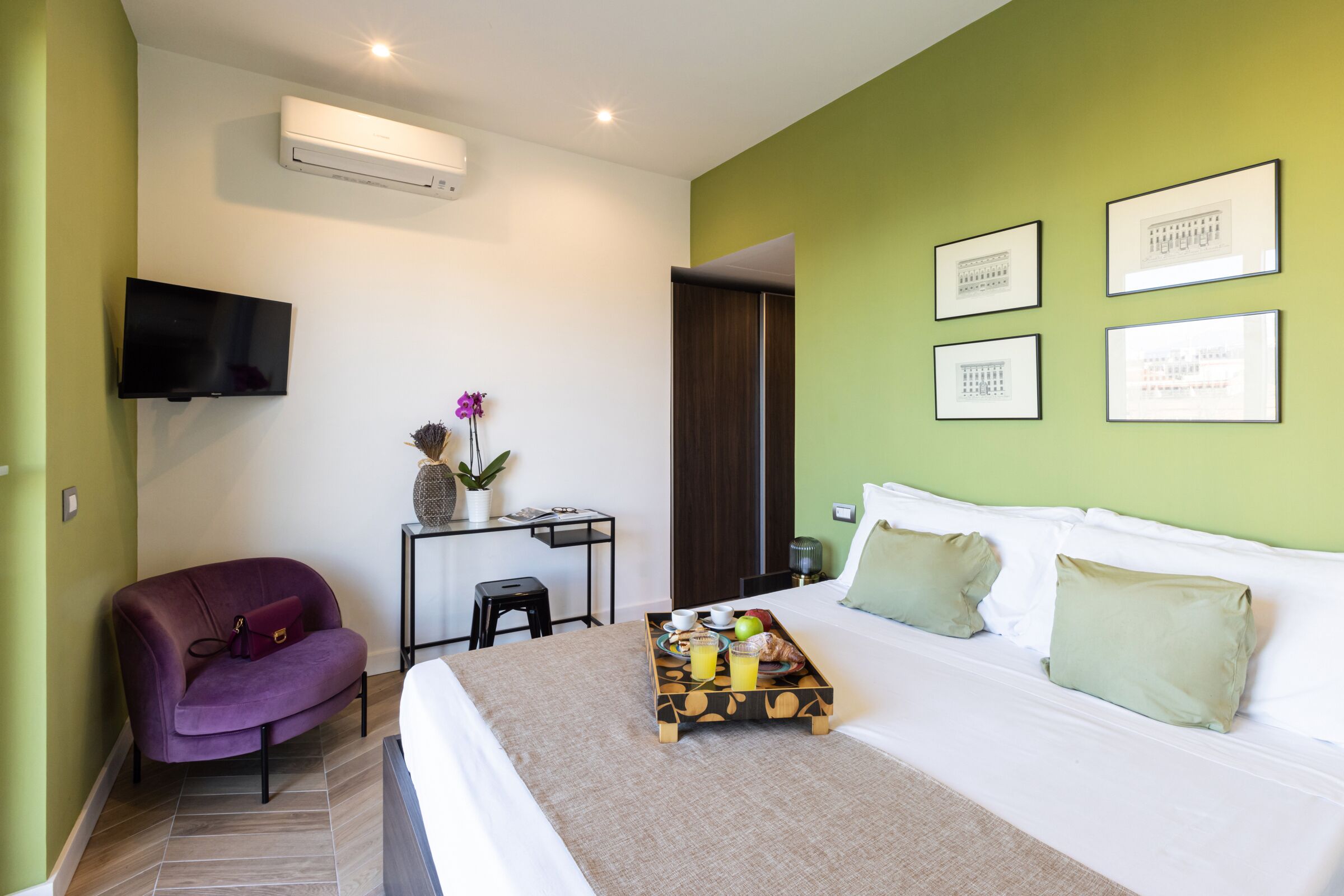 A hotel room with a bed, a desk with a chair, a television, and a wall-mounted air conditioner.