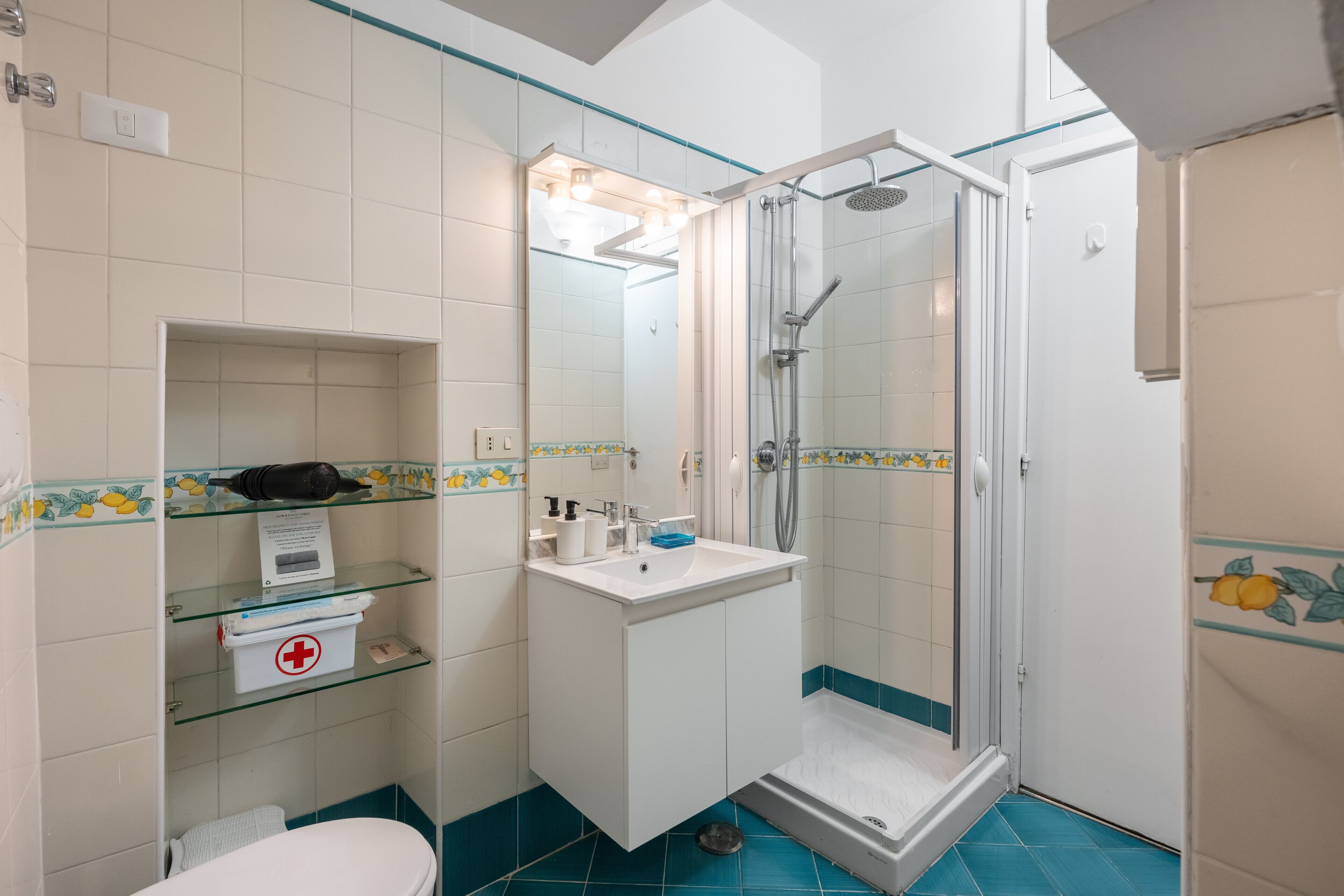 Un baño con ducha, inodoro y repisa de vidrio con artículos de aseo.