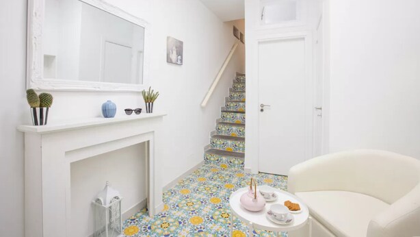 A hallway with a white fireplace, a mirror, a staircase with floral tiles, and a white armchair. - Brezza Marina-Authentic Sorrento Flat By The Beach (Sorrento)