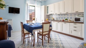 Un coin repas avec une table dressée pour quatre personnes, une cuisine avec des meubles blancs et un four à micro-ondes, et un téléviseur fixé au mur.