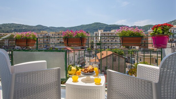 Un balcon avec des fauteuils en osier, une table où est servi le petit-déjeuner et des plantes en pot.