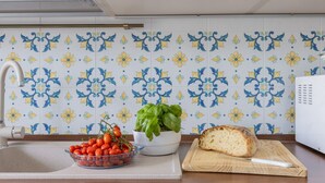 Une cuisine avec un mur recouvert de carreaux, un saladier de tomates cerises, un plant de basilic et un pain sur une planche à découper.