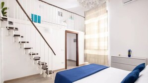 A modern bedroom with a staircase, a bed with blue bedding, a nightstand, and a window with sheer curtains. - Cosy House Under The Arches In Sorrento Old Town (Sorrento)